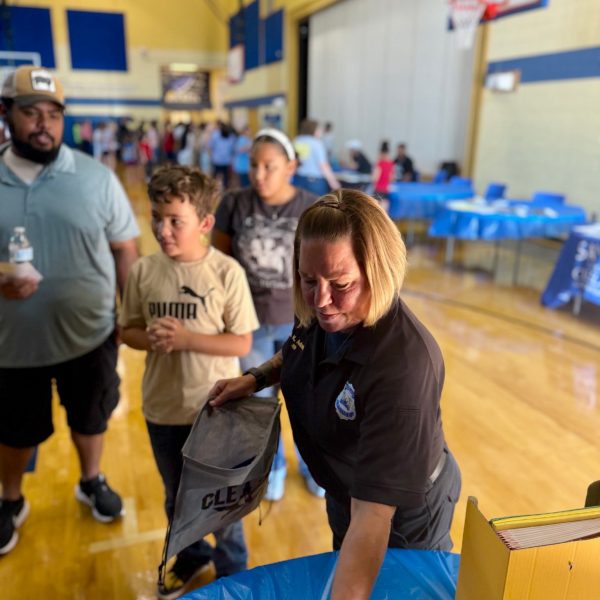 An officer hands out school supplies to children and families at a table inside the RG Jones School gym.