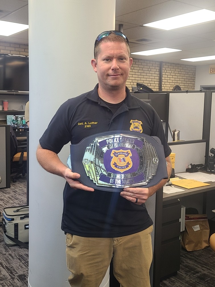 Detective Aaron Luther stands inside the Second District office holding a Cleveland Police Officer of the Month award belt.
