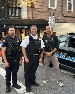 Three Cleveland Police officers stand smiling on Mayfield Road in front of Etna Ristorante during the Feast of the Assumption.