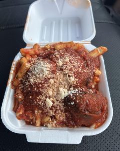 A takeout container filled with baked ziti topped with tomato sauce, meatballs, and grated cheese at the Feast of the Assumption.