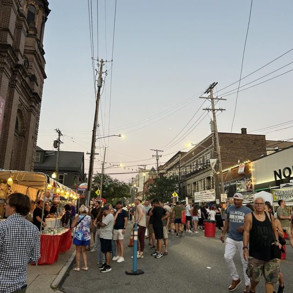 Festival-goers stroll past food stands and vendor tents along Mayfield Road as the evening sky sets over Little Italy.