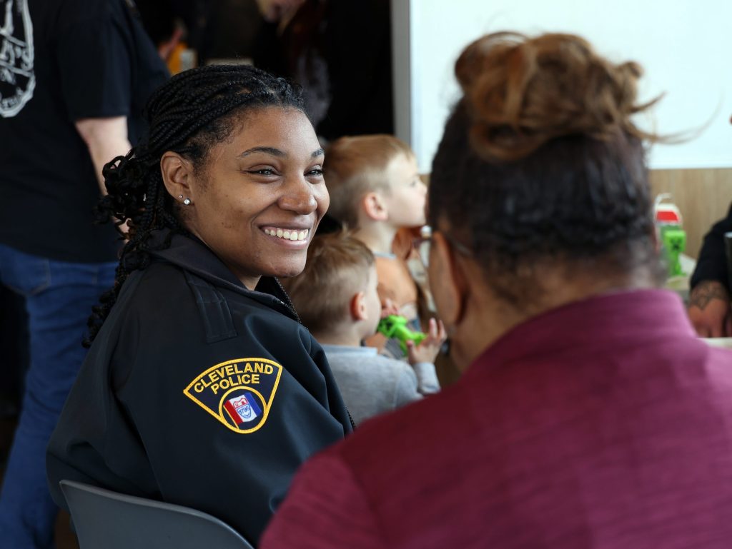 A Cleveland police officer smiles while speaking with a community member at a gathering with children in the background.