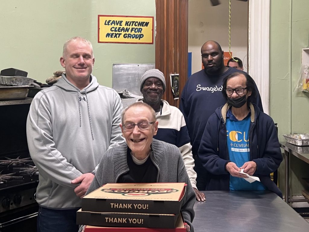 Residents and staff in a group home kitchen hold donated pizzas from local police officers, ready to share a meal together.