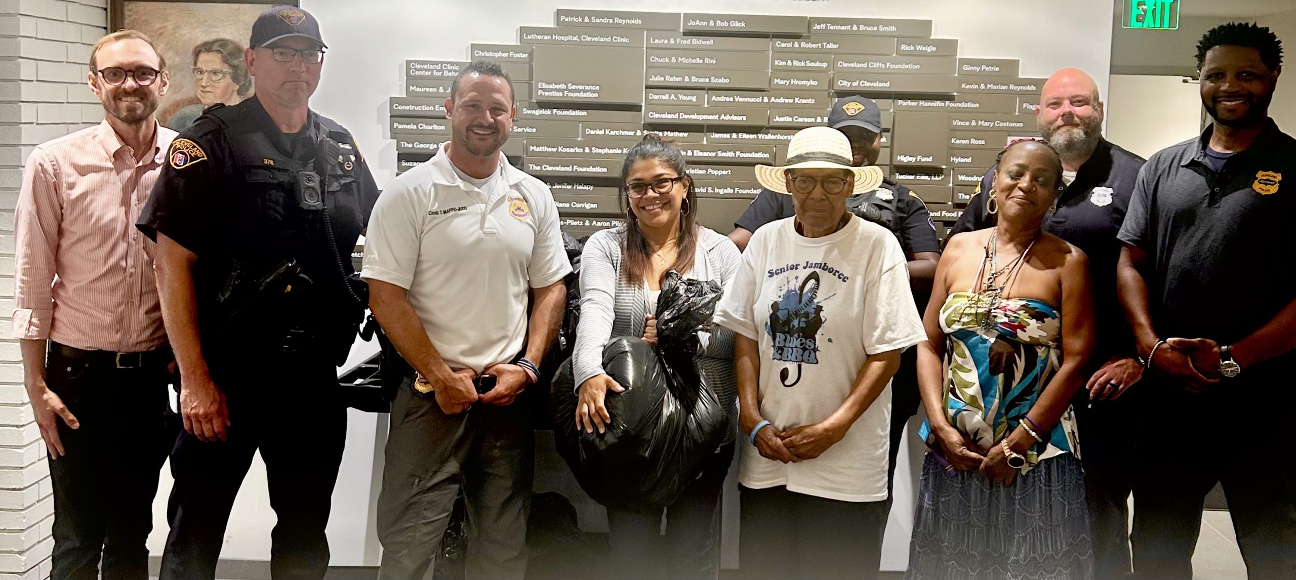 Second District officers, community partners, and May Dugan Center staff stand together with donated clothing bags, celebrating the contribution.