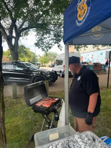 A Cleveland Police officer grills rows of hot dogs on an outdoor grill under a tent as part of the Fairfax National Night Out celebration.