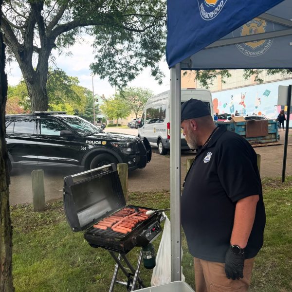 A Cleveland Police officer grills rows of hot dogs on an outdoor grill under a tent as part of the Fairfax National Night Out celebration.