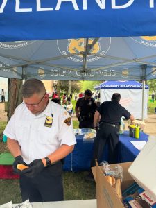 A Cleveland Police officer prepares a hot dog under a department tent while other officers work at a nearby table during National Night Out.