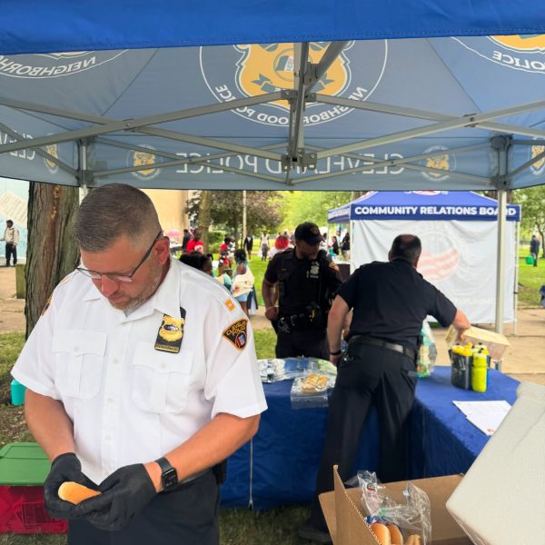 A Cleveland Police officer prepares a hot dog under a department tent while other officers work at a nearby table during National Night Out.