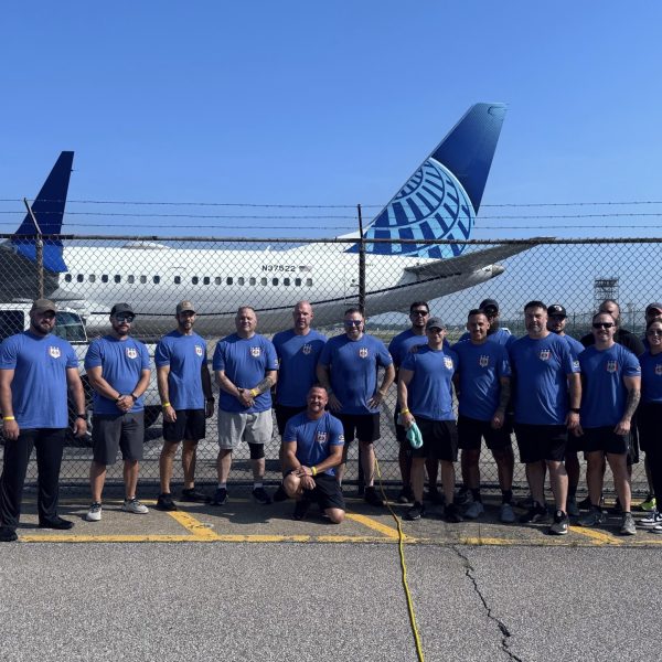 The Cleveland Police Plane Pull team poses in blue shirts in front of a United Airlines plane after competing.