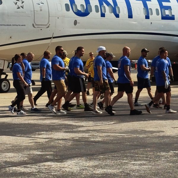 Second District officers and teammates in matching blue shirts walk past a United Airlines jet on the tarmac before their pull.