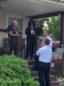 Two Cleveland Police officers stand at the base of a porch speaking with two women, one holding notes, during the Third District safety walk.