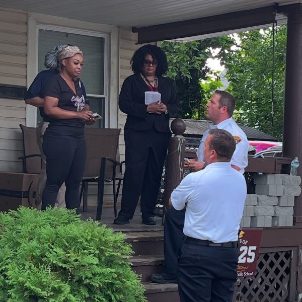 Two Cleveland Police officers stand at the base of a porch speaking with two women, one holding notes, during the Third District safety walk.
