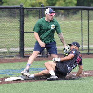 Player in a green shirt attempts to tag out a sliding runner in a black Cleveland Police softball jersey at third base.