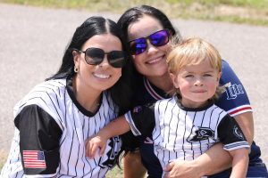 Two women and a young boy, all wearing baseball-style jerseys, smile for the camera at the Police/Fire softball game.