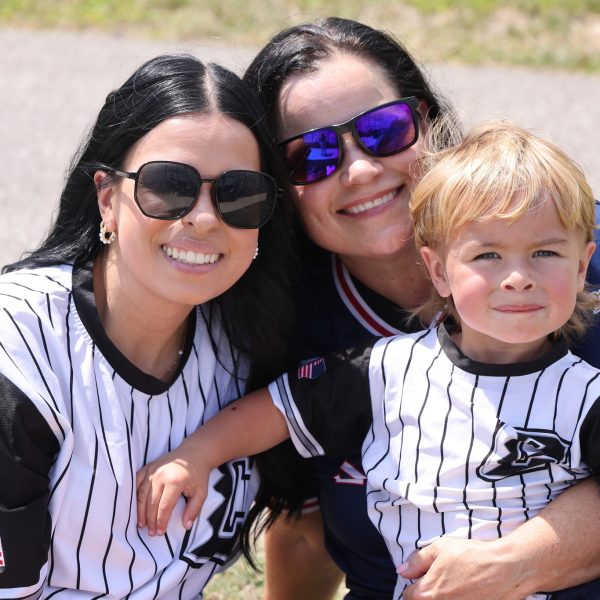 Two women and a young boy, all wearing baseball-style jerseys, smile for the camera at the Police/Fire softball game.