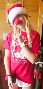 Young volunteer dressed festively in a Santa hat and red nose, smiling at the camera.