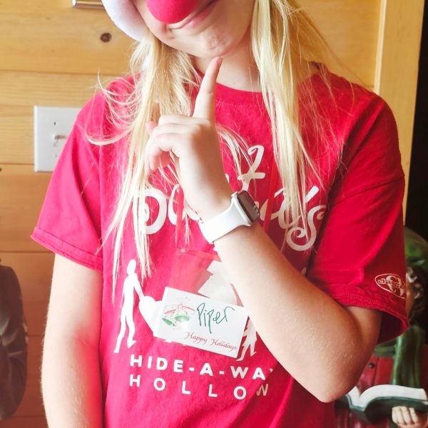 Young volunteer dressed festively in a Santa hat and red nose, smiling at the camera.