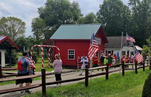 Parade of children and volunteers, some dressed as elves, walking past the North Pole Town Hall decorated with American flags and candy canes.
