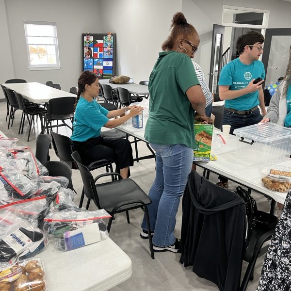 Volunteers in teal shirts prepare donation bags with snacks and supplies inside a community space.