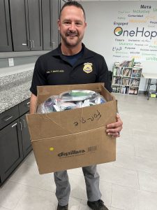 Second District Commander Tim Maffo-Judd smiles while holding a box of packed donation bags at OneHope NEO.