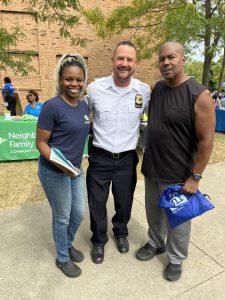 Officer posing with two community members in front of a resource table.