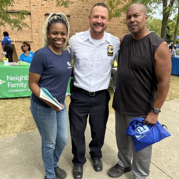 Officer posing with two community members in front of a resource table.