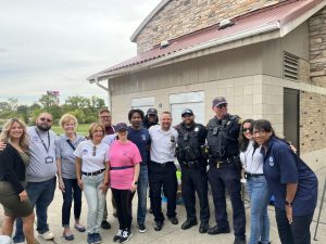 Group photo of officers, volunteers, and community partners smiling together outside the pavilion.