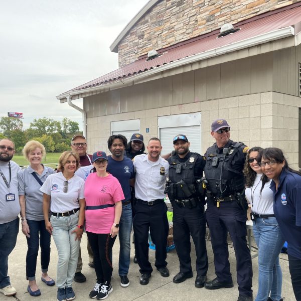 Group photo of officers, volunteers, and community partners smiling together outside the pavilion.