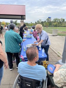 Volunteer handing out food and drinks at a long community table covered in blue cloth at Michael Zone Rec Center.
