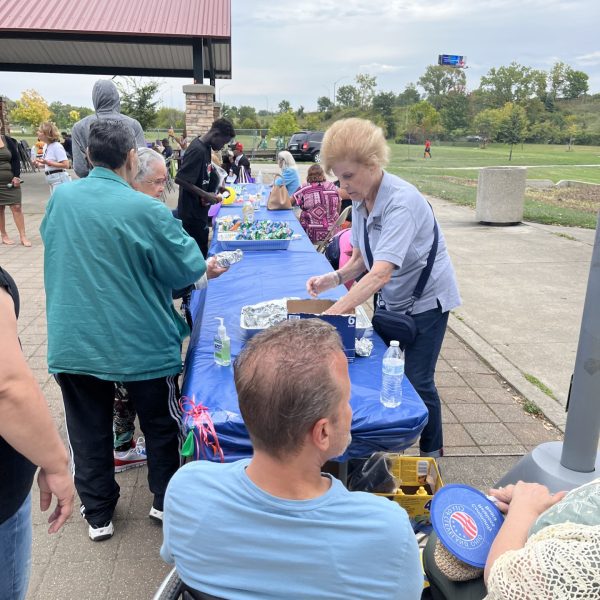 Volunteer handing out food and drinks at a long community table covered in blue cloth at Michael Zone Rec Center.