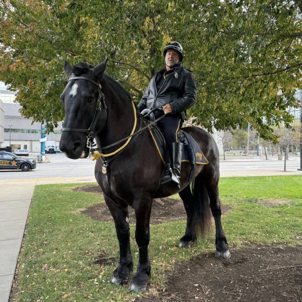 Officer George Janusczak on horseback beneath fall foliage, wearing a leather jacket and helmet.