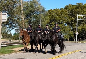 Four Cleveland Police Mounted Unit officers riding in formation on a sunny day.