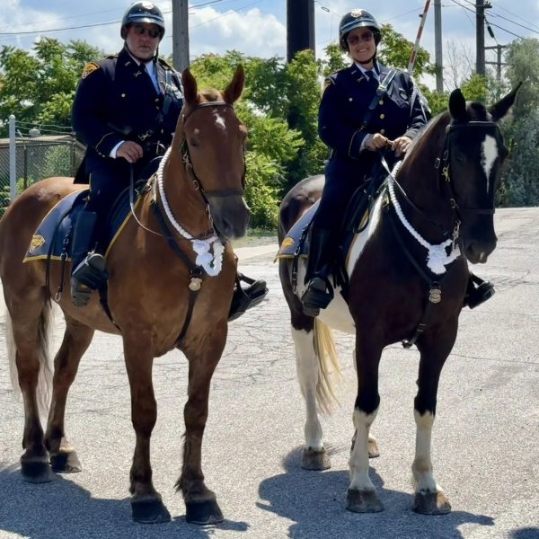 Officer Janusczak and a fellow officer smiling while mounted on horses outdoors.