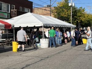 Festivalgoers walking under a large white tent with food and community tables set up.