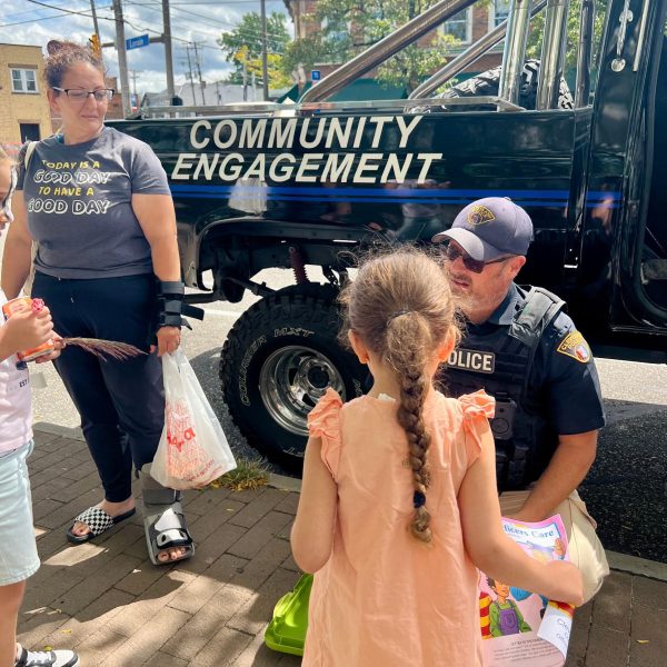 Officer handing out materials to children next to the CPD Monster Truck with “Community Engagement” painted on the side.