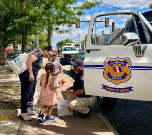 Officer kneeling to hand out treats and coloring books beside the CPD Monster Truck, speaking with children and parents.