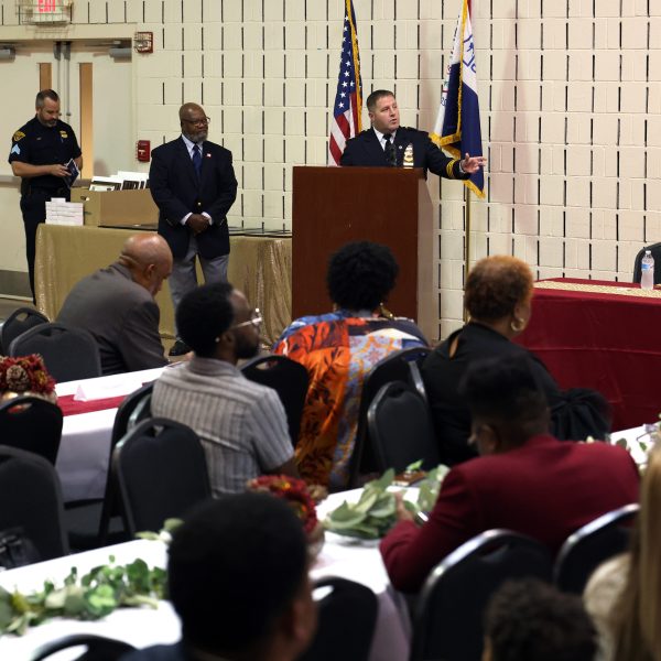 Commander Mark Maguth speaking at the podium, with Harry Boomer and others on stage.