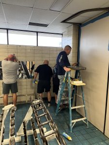 Volunteers painting and repairing a wall inside the Fifth District gym as part of the renovation effort.