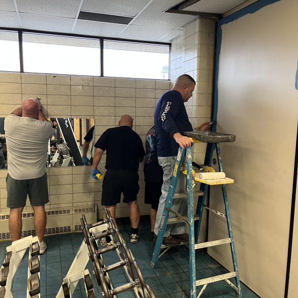 Volunteers painting and repairing a wall inside the Fifth District gym as part of the renovation effort.