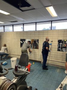 Volunteers cleaning mirrors and scrubbing equipment inside the Fifth District gym during the renovation effort.