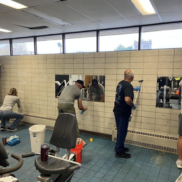 Volunteers cleaning mirrors and scrubbing equipment inside the Fifth District gym during the renovation effort.