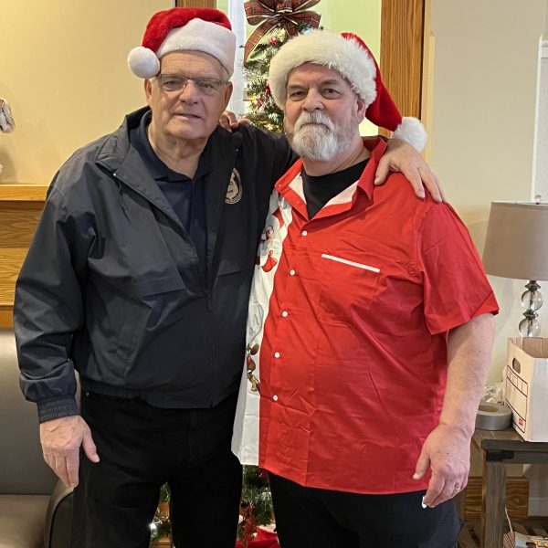 Two volunteers wearing Santa hats pose together inside the Ronald McDonald House during the Cops, Kids and Christmas event.