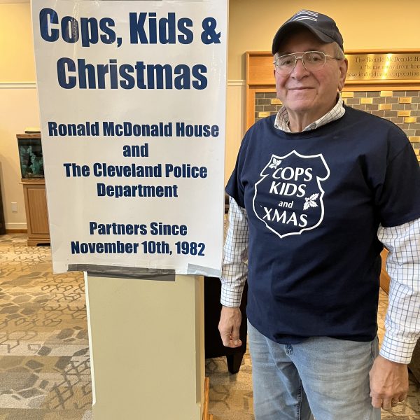 A volunteer stands next to a sign recognizing the long-running partnership between the Cleveland Police Department and the Ronald McDonald House.