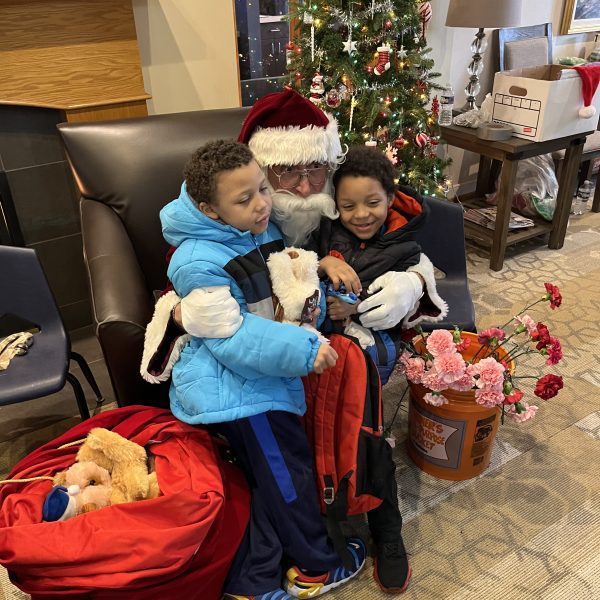 Santa Claus sits with two children while distributing gifts during the Cops, Kids and Christmas event at the Ronald McDonald House.