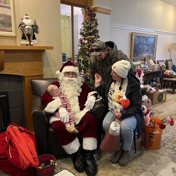 Santa Claus sits with a family and a baby during the Cops, Kids & Christmas event at Ronald McDonald House.