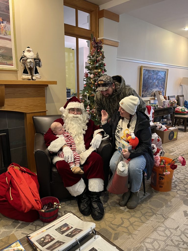 Santa Claus sits with a family and a baby during the Cops, Kids & Christmas event at Ronald McDonald House.