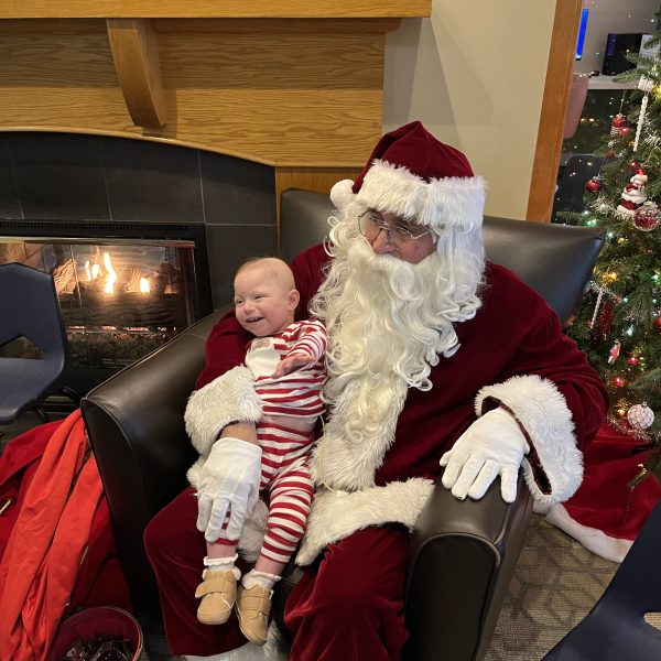 Santa Claus holds a smiling baby near a fireplace during the Cops, Kids & Christmas visit at Ronald McDonald House.
