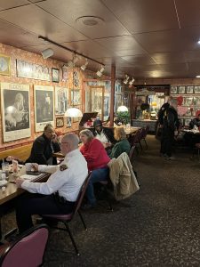 Community members and police officers seated at tables inside a restaurant, talking over coffee during a Coffee with a Cop event.