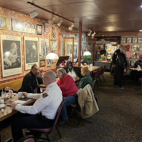 Community members and police officers seated at tables inside a restaurant, talking over coffee during a Coffee with a Cop event.