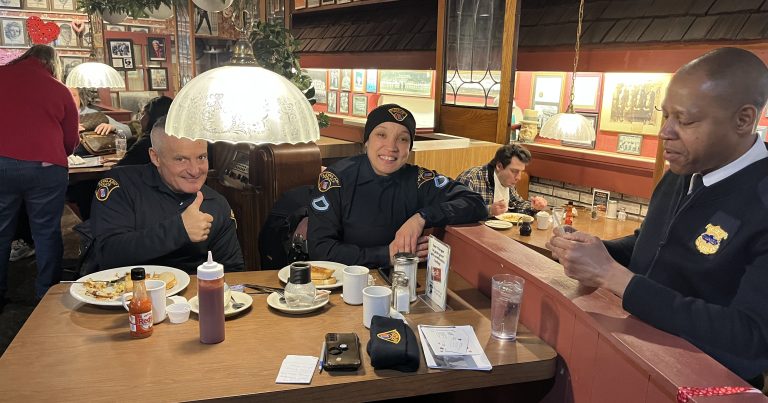 Police officers seated at a restaurant counter and booth, smiling and talking over breakfast during a Coffee with a Cop gathering.